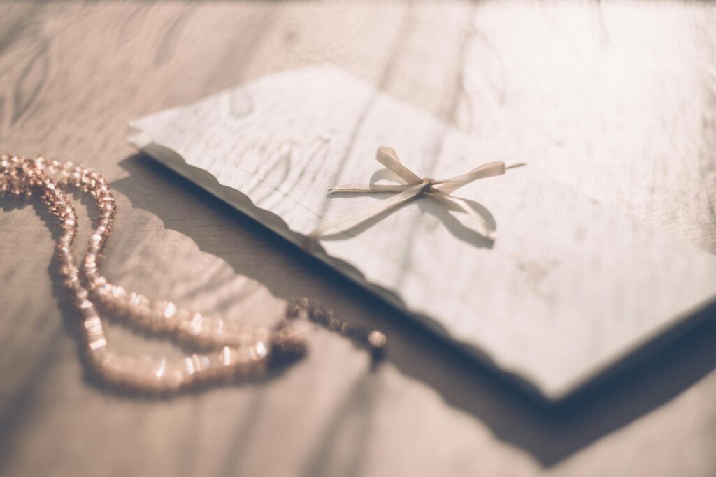 Elegant envelope with delicate bow placed on a sunlit wooden table, perfect for special occasions.